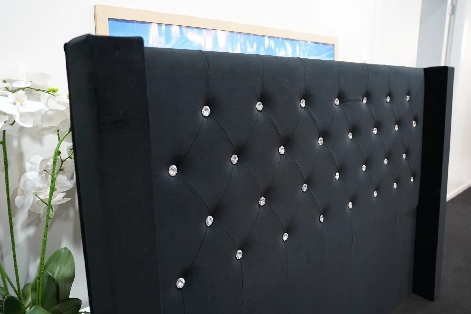 A black velvet winged headboard, deep buttoned with crystal buttons, standing in the workshop.