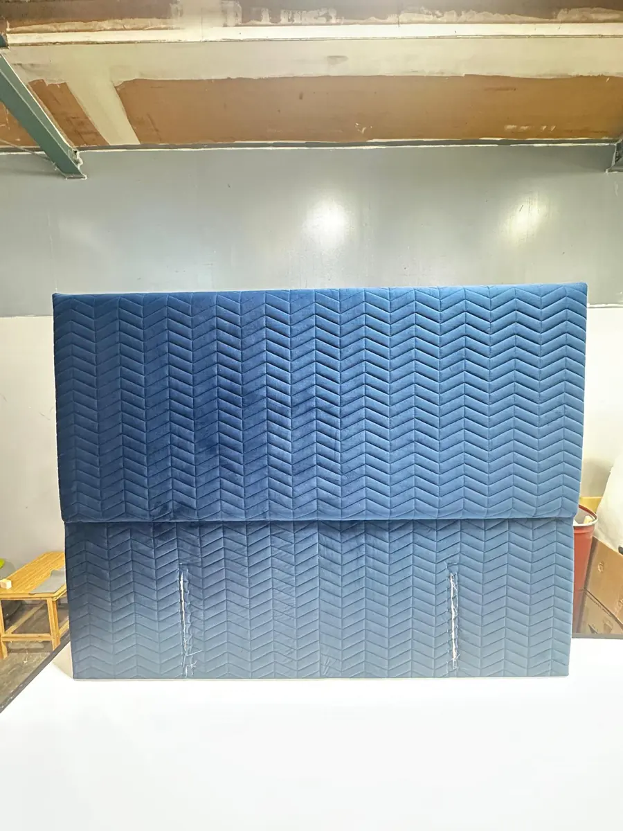 A blue velvet headboard with a chevron-stitched face, freshly finished in the workshop.