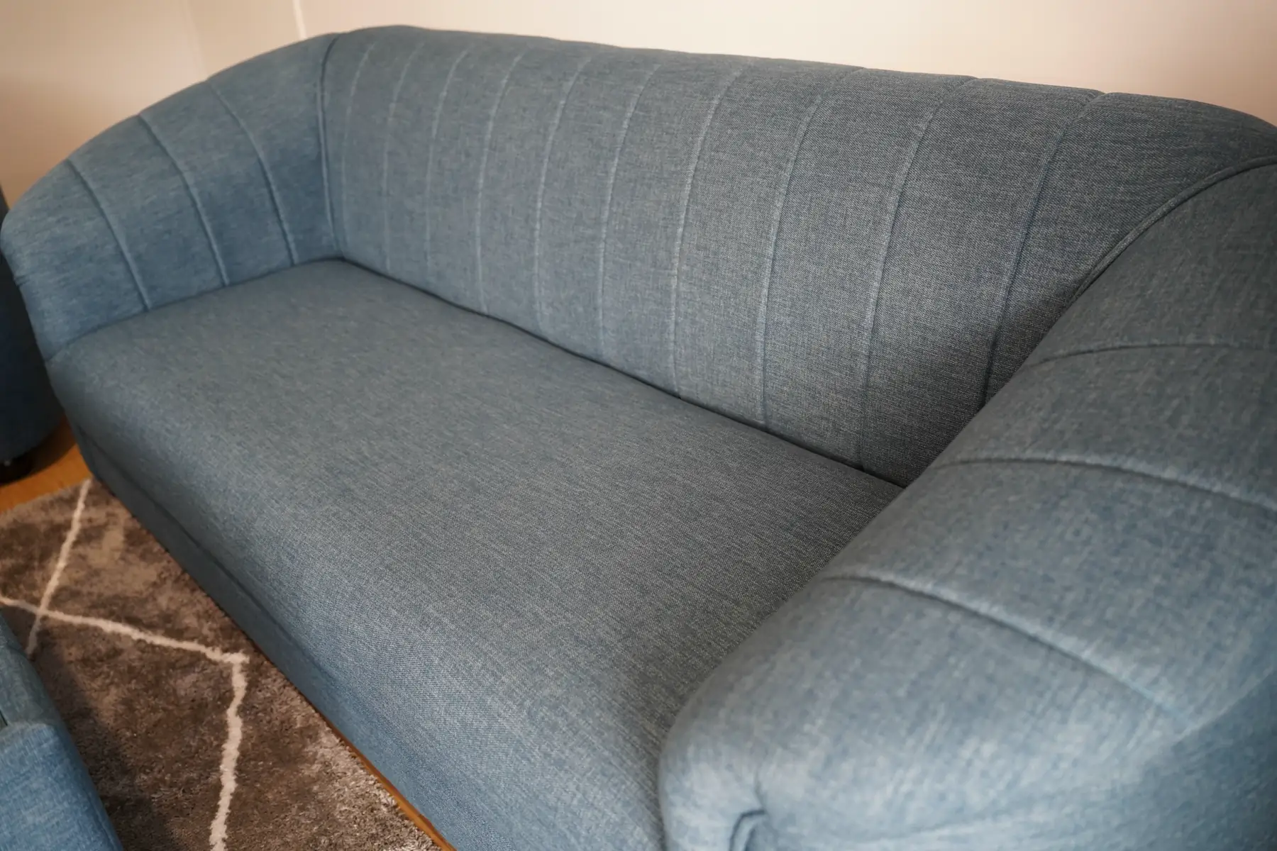 Close on a blue-grey sofa with vertical fluting running up the back and rolled arms.