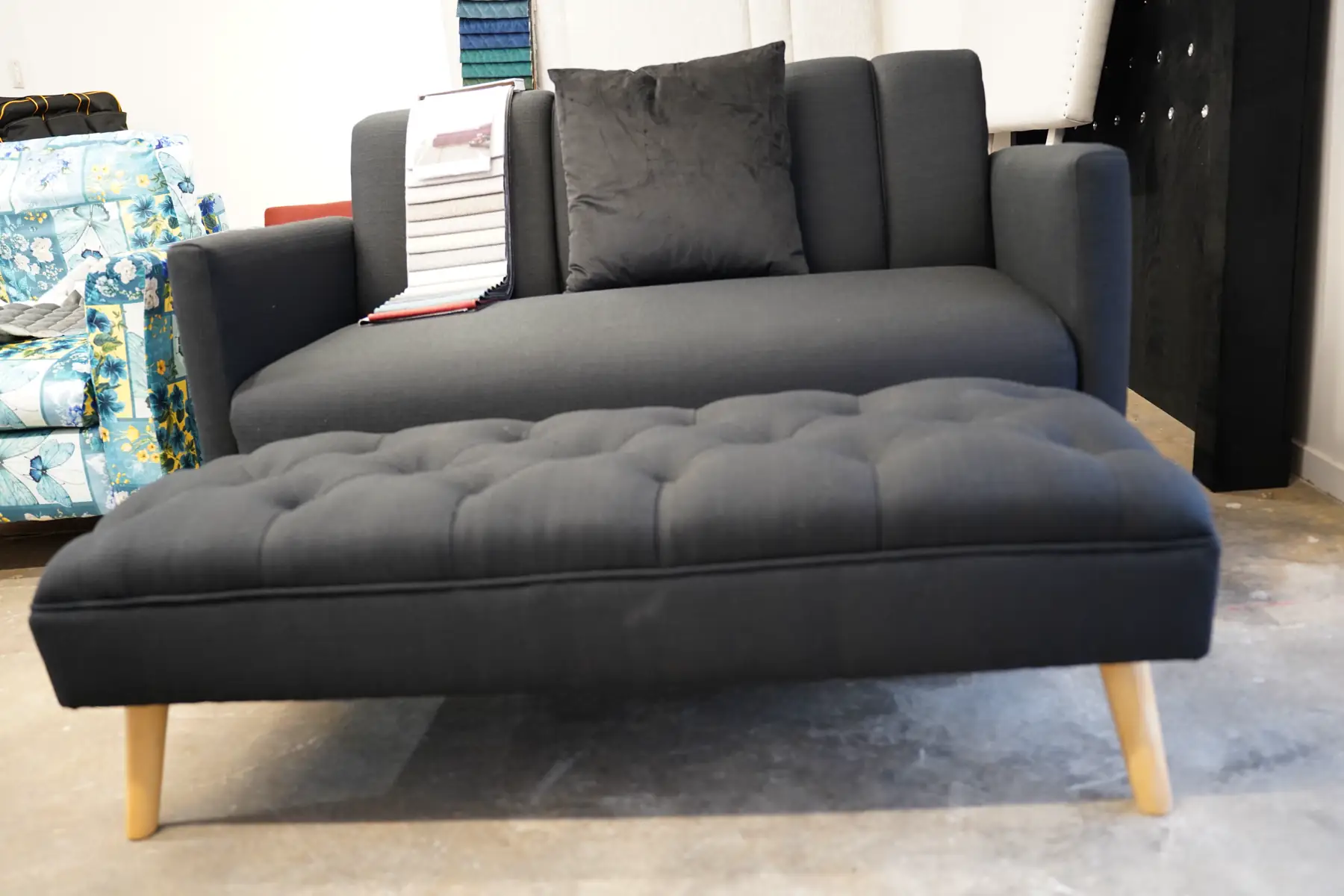 A charcoal chaise with a buttoned seat, on pale tapered legs.