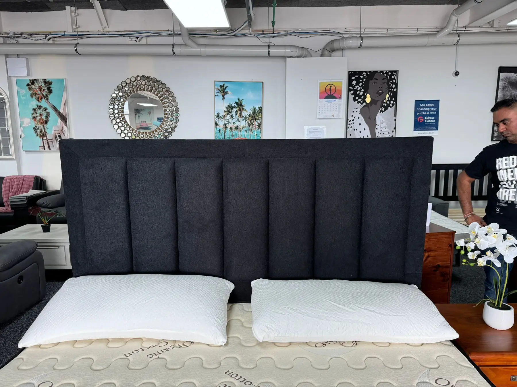 A wide charcoal panelled headboard behind a mattress in the showroom.