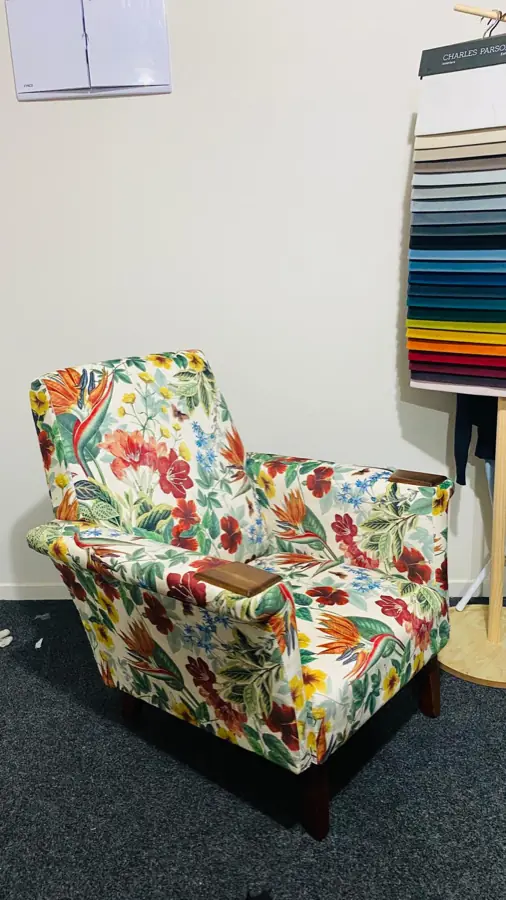 A small armchair recovered in a bright botanical print, beside a stack of fabric samples.