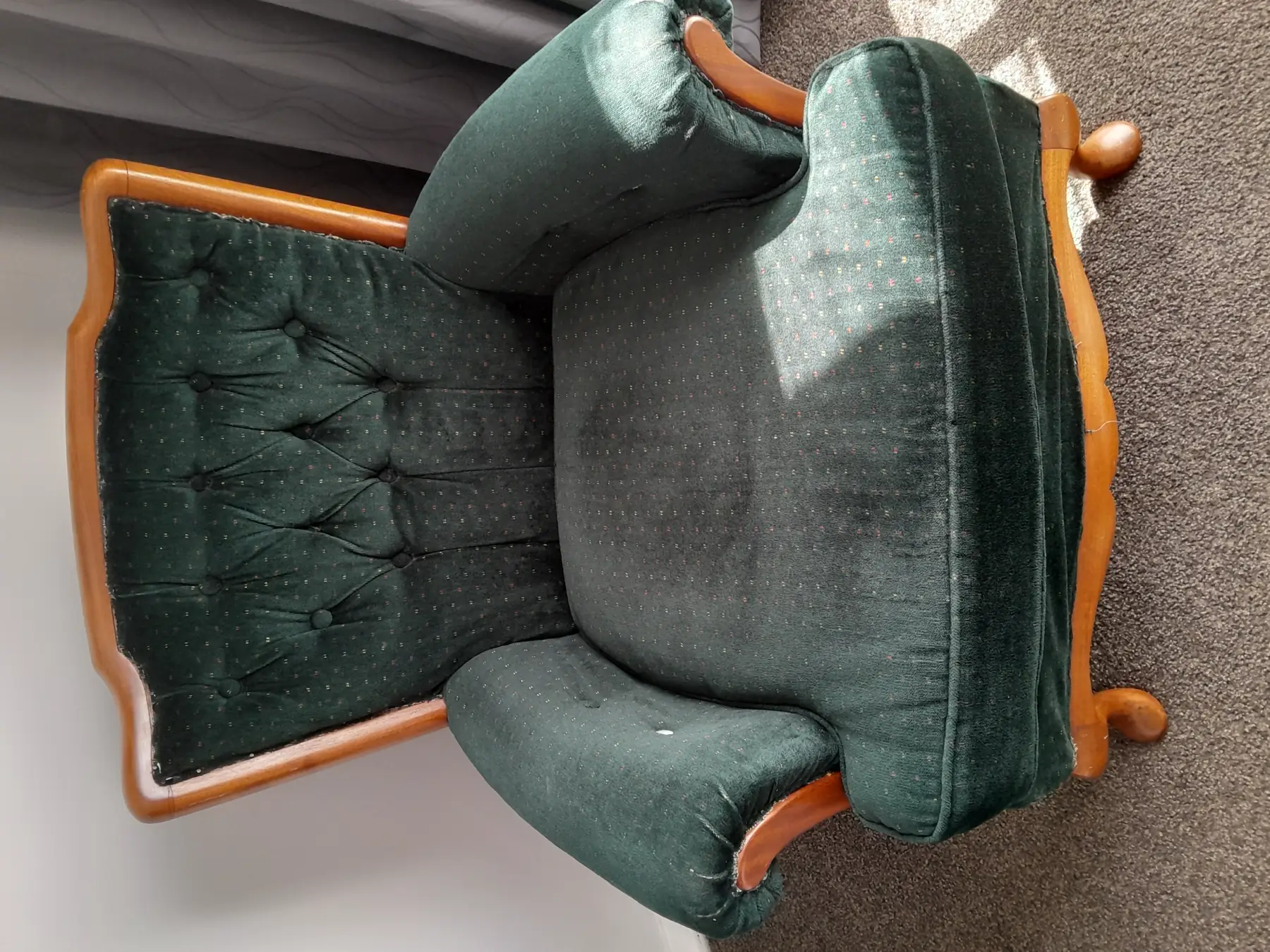 A deep green velvet armchair with a carved timber frame and buttoned back, before work.