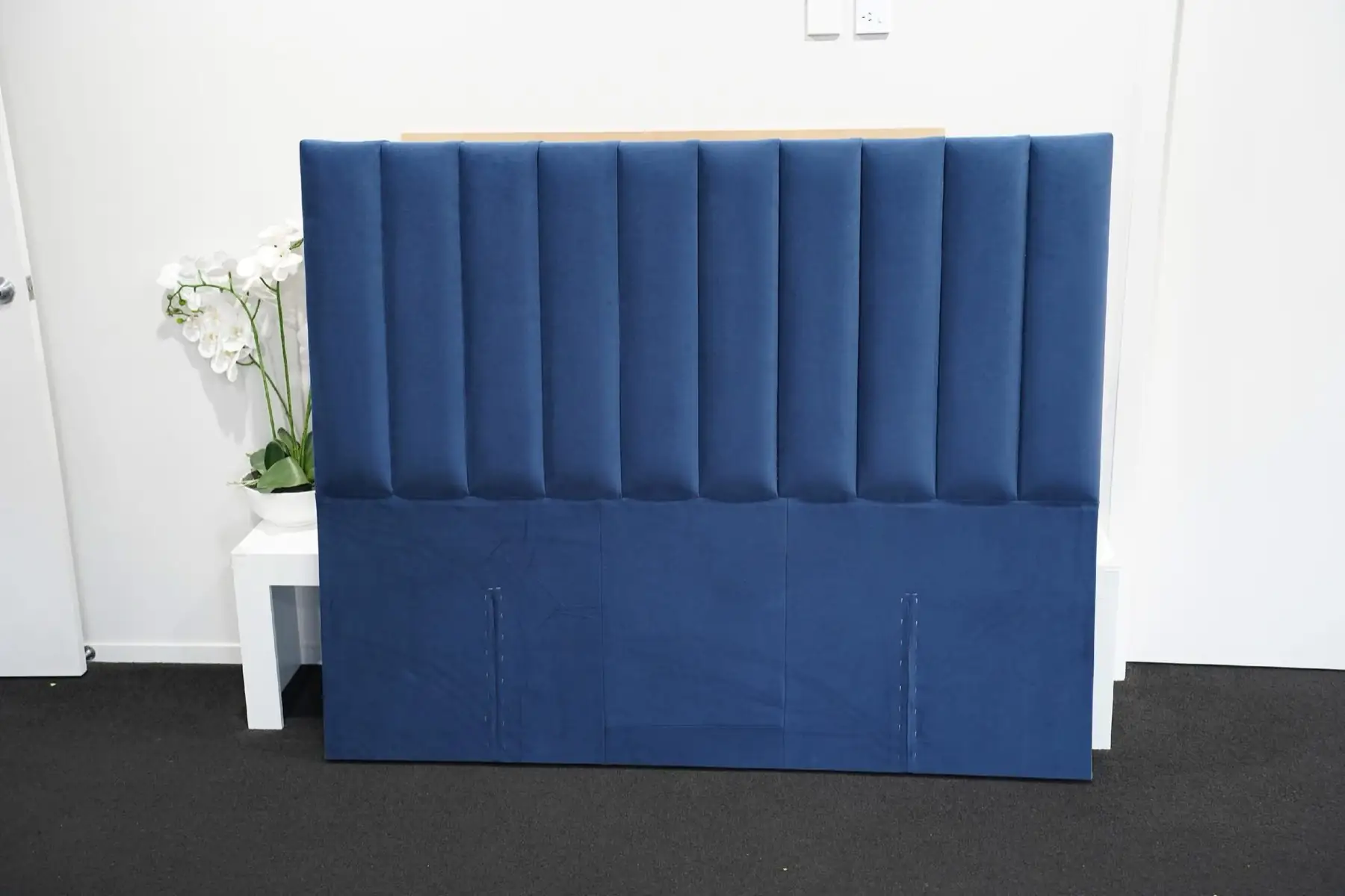 A navy headboard with tall vertical flutes, standing against a white wall.