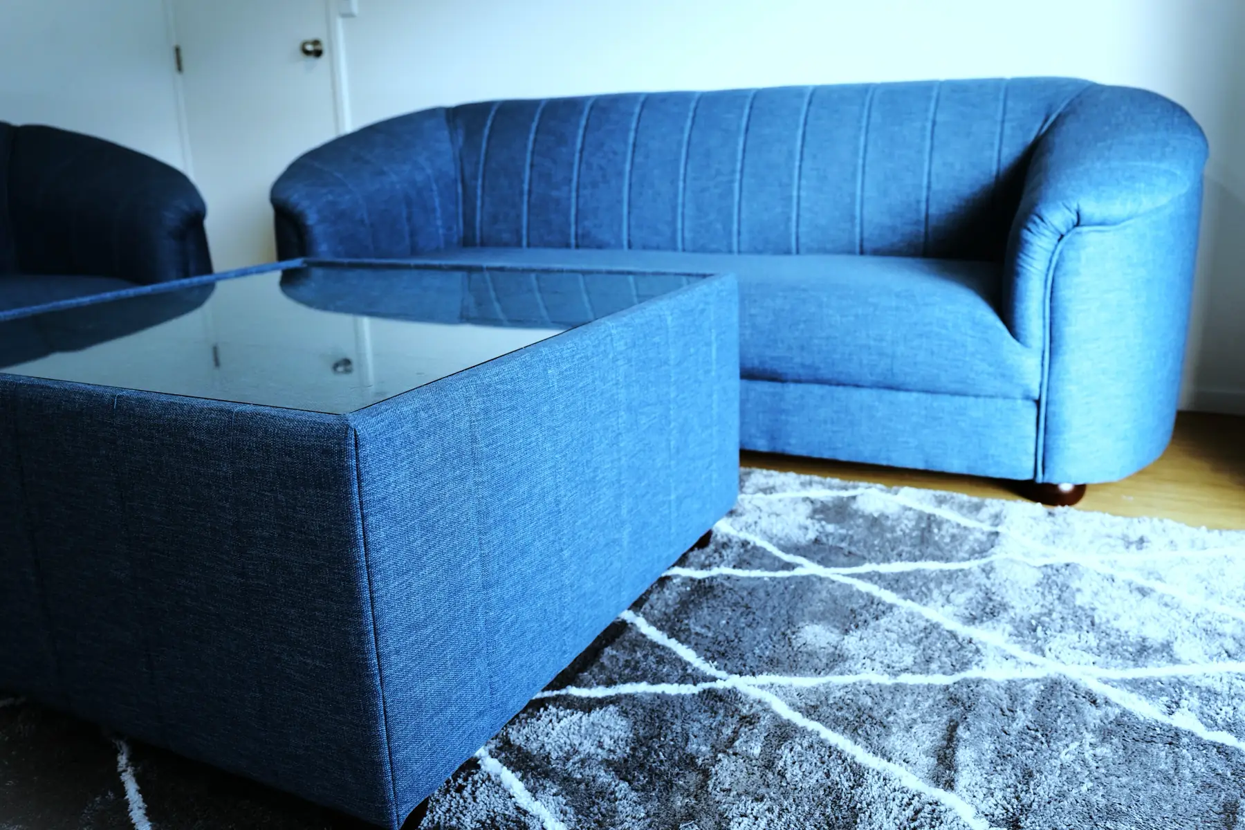 A navy fluted sofa with a matching glass-topped ottoman on a patterned rug.