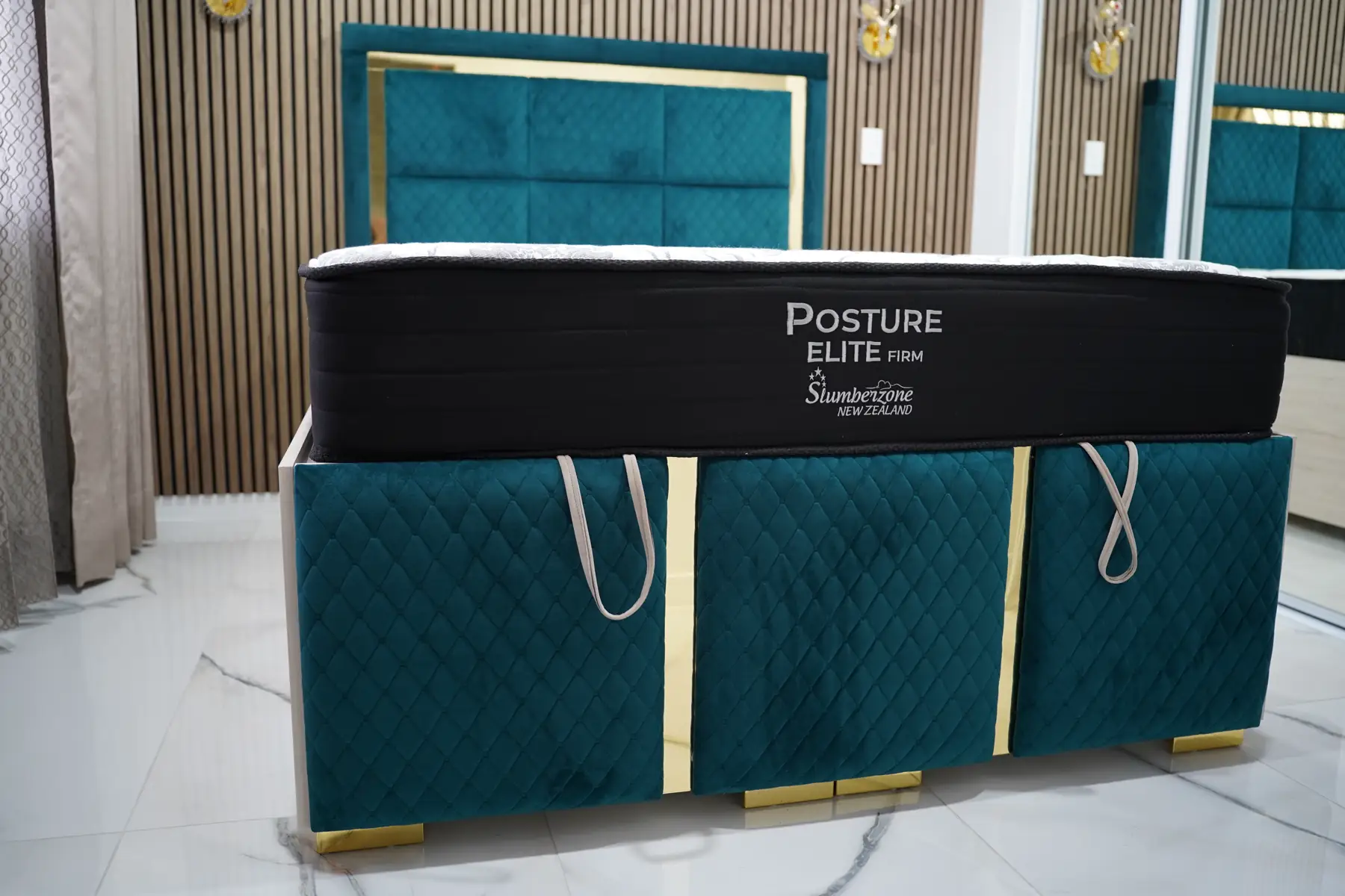 A teal velvet bed base with gold feet and pull handles on the storage drawers.