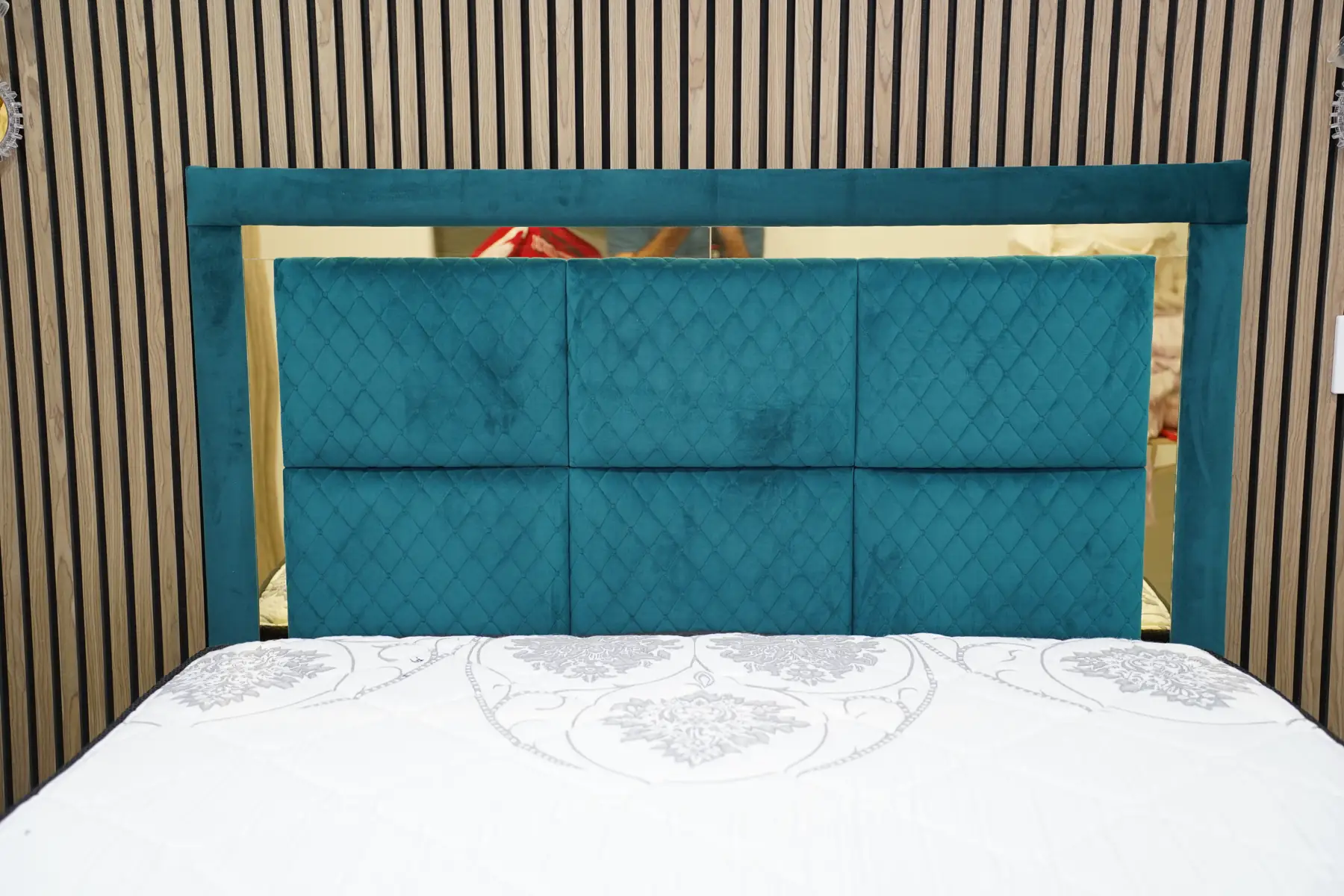 A teal velvet headboard with a brushed gold frame, panelled and diamond-quilted, against a slatted timber wall.
